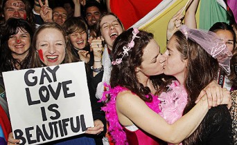 CHRIS SKELTON/Fairfax NZ LOVING SUPPORT: Rosie Jimson-Healey holds a sign as Emma Fawcett and Phillipa Walker kiss during a rally outside Parliament as the Marriage (Definition of Marriage) Amendment Bill is debated inside.